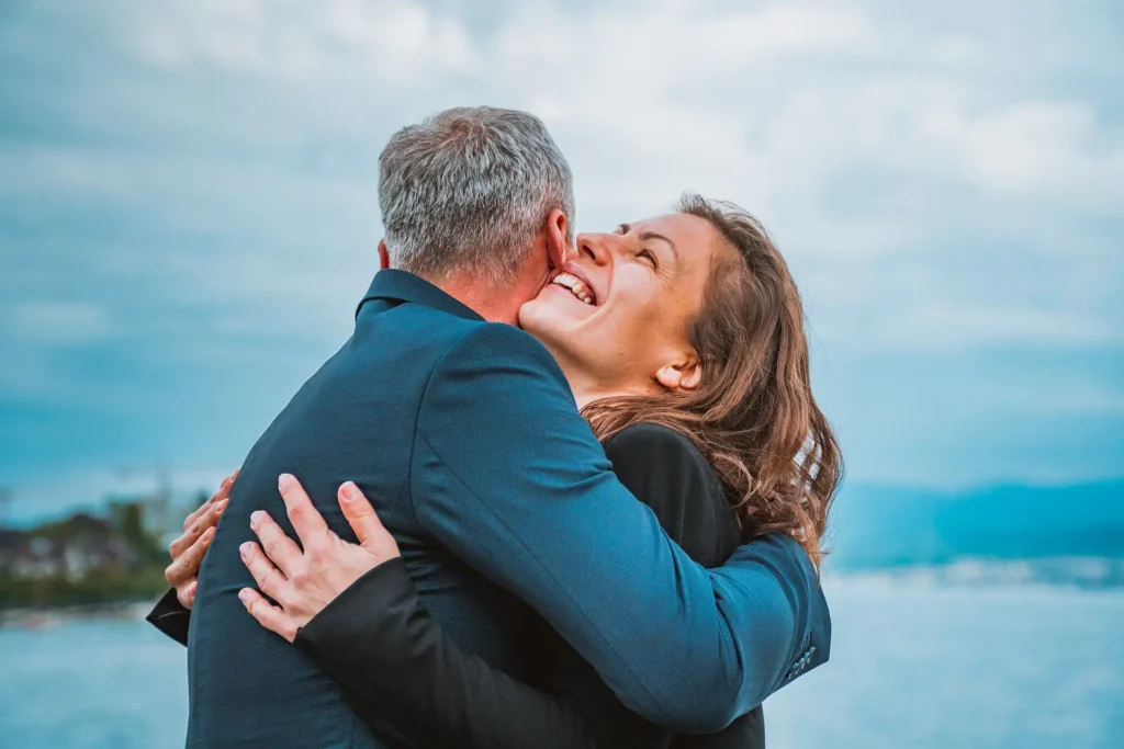 A couple embraces in front of a lake.